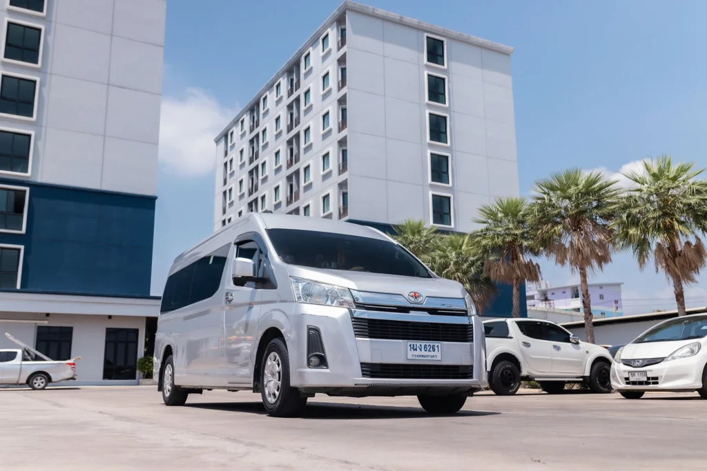 ภาพด้านหน้าเฉียงของรถตู้ Toyota Commuter พร้อมให้บริการเช่ารถตู้ VIP ที่จอดอยู่หน้าโรงแรม Cozy Blu